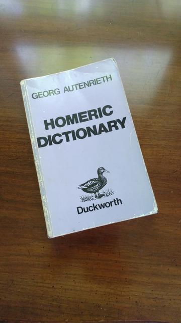 A well-worn book with a light gray cover on a wooden table. The author is Georg Autenrieth, and the title is "Homeric Dictionary." There is also the word "Duckworth" (the publisher) with a line drawing of a duck.