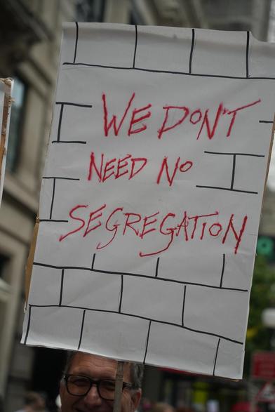 A protest sign that says "We don't need no segregation" written over a hand drawn brick wall texture.