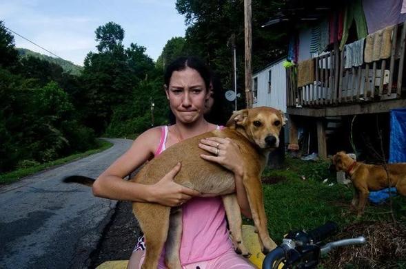 devant la maison, la femme au chien, le visage crispé, serre l’animal contre sa poitrine