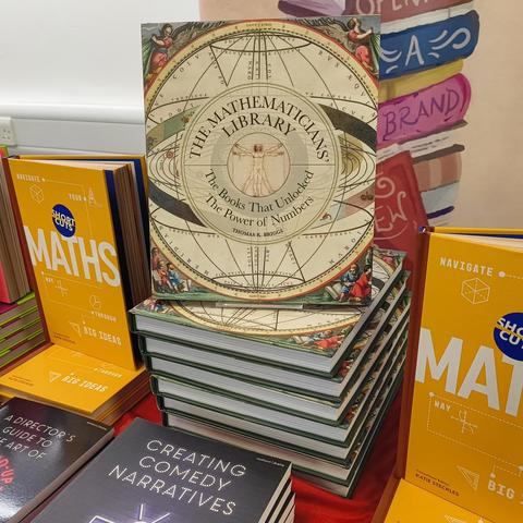 A copy of my book, The Mathematicians' Library, stands upright on a pillar of seven other copies stacked on top of each other. They are flanked by other maths-themed books.