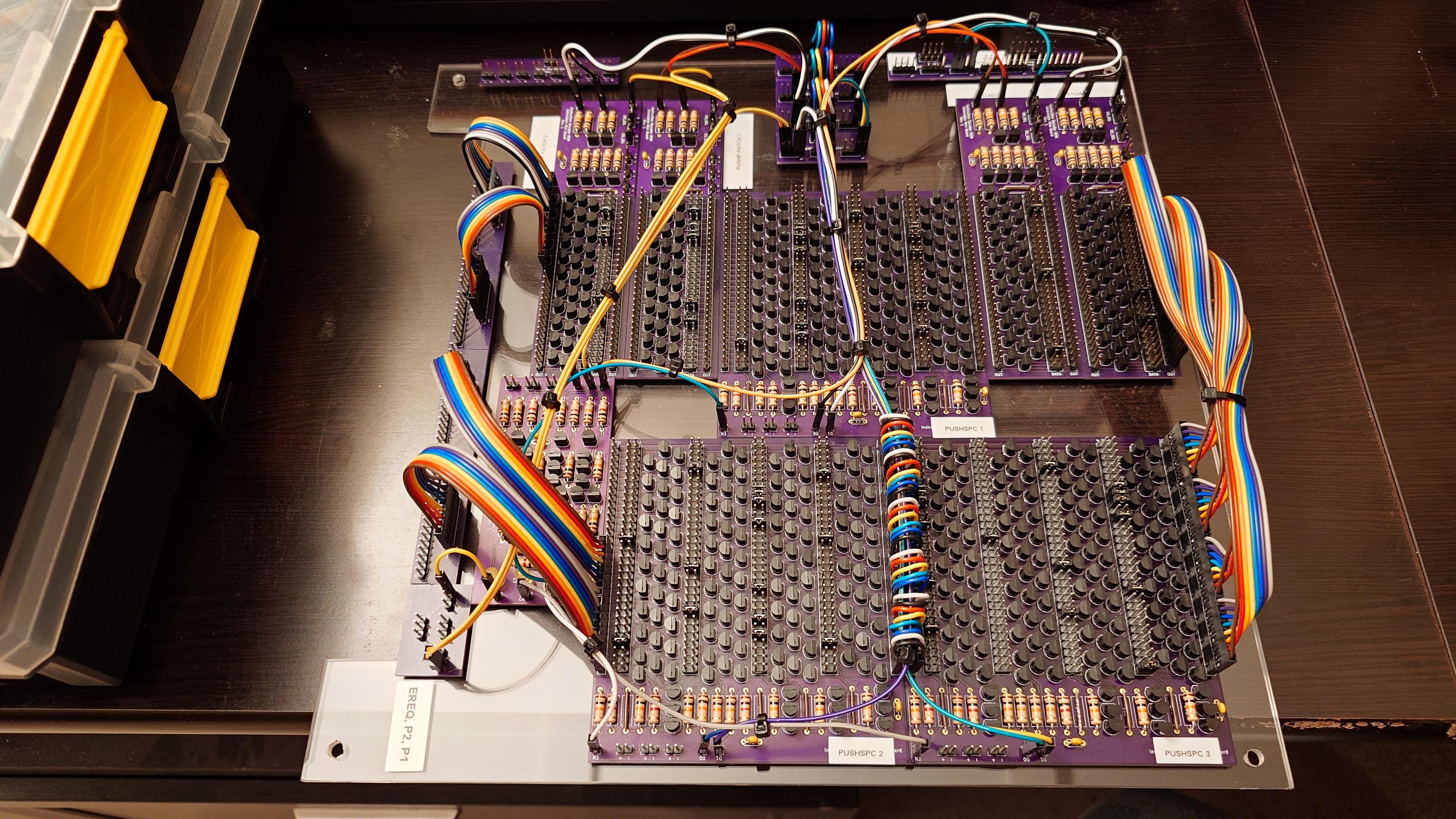 A one square foot acrylic panel that's got holes drilled in the four corners for standoffs. Attached to it is an array of PCBs that are wired to each other. There's some labeling on the board for which PCB corresponds to what instruction. The wires that are present are zip-tied together to apply some semblance of cable management.